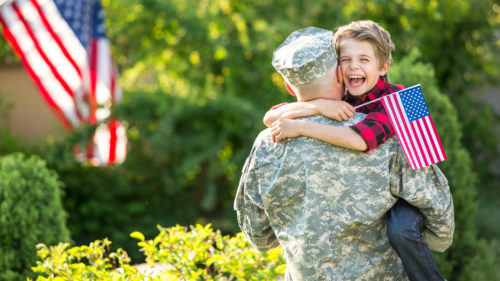 Military man holding smiling young boy who holds a flag