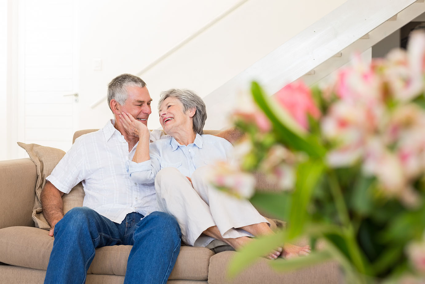 Elderly couple sitting on a couch with a bouquet of flowers blurry in the foreground