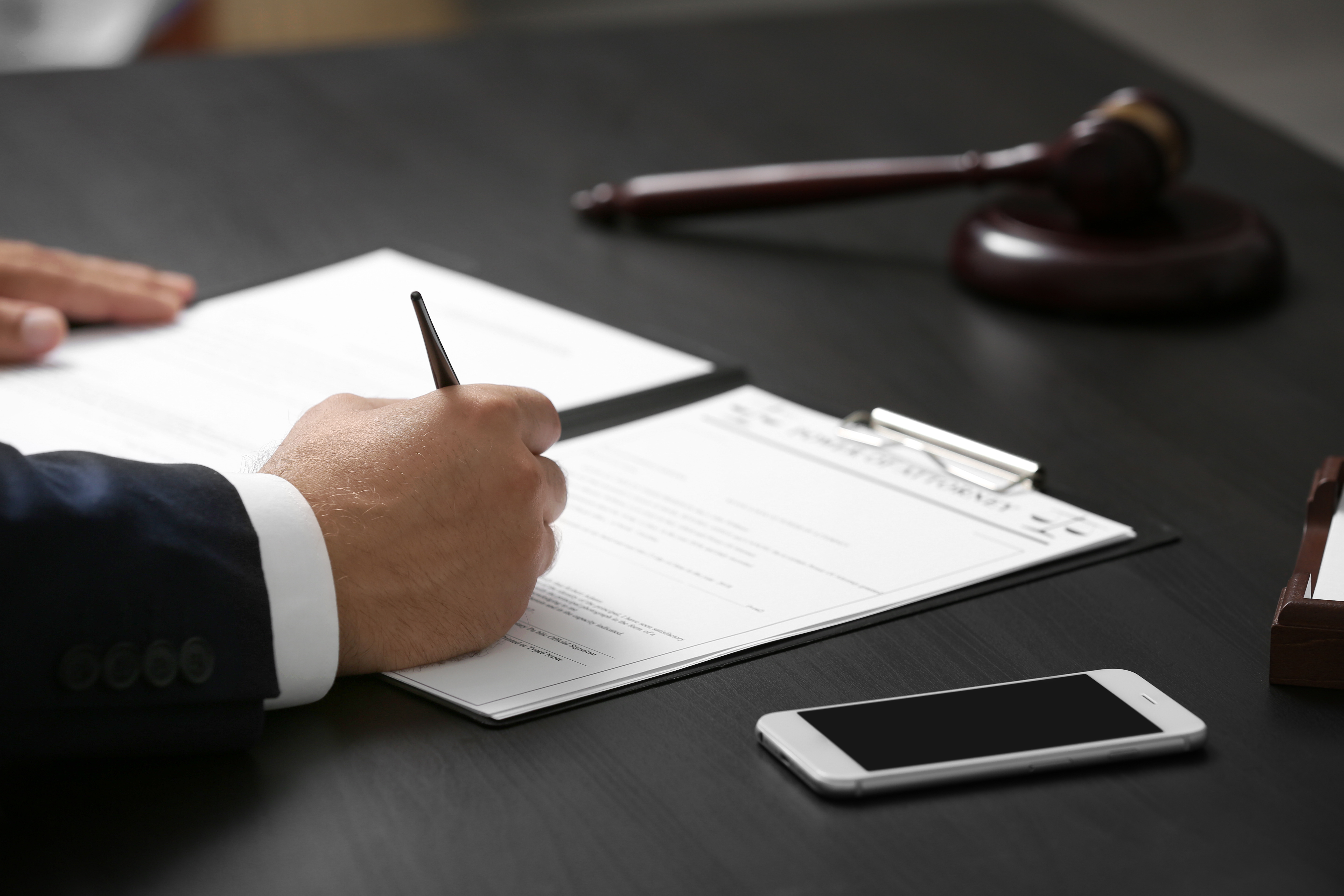 Man signing legal paperwork with gavel on the table