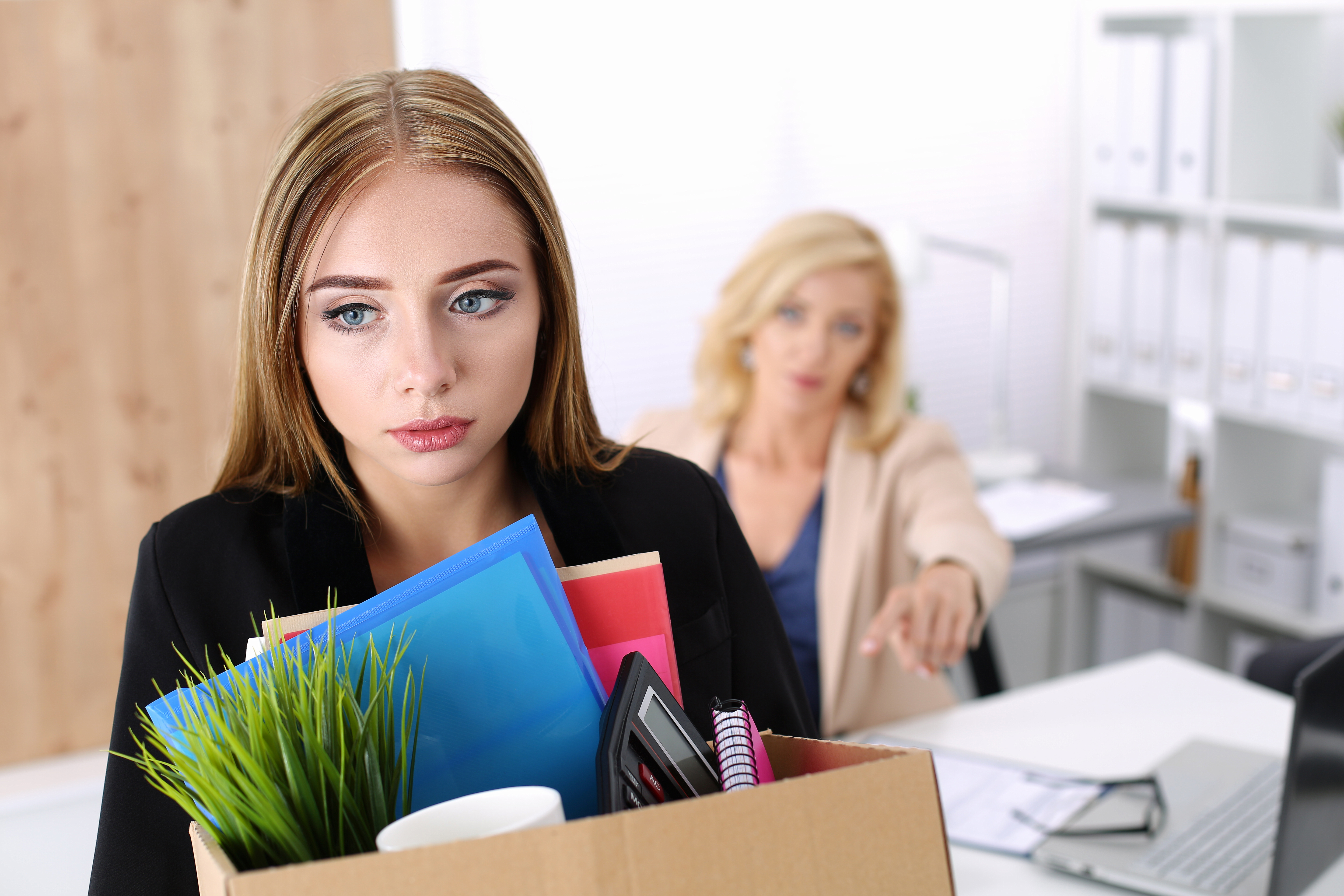 Woman being fired and taking her desk belonging out of the office in a cardboard box